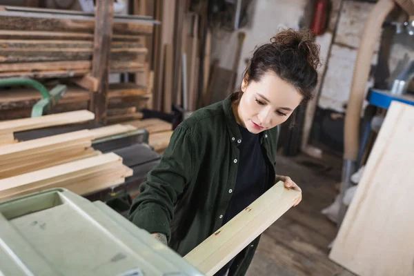 Brunette menuisier tenant planche en bois près de raboteuse épaisseur — Photo de stock