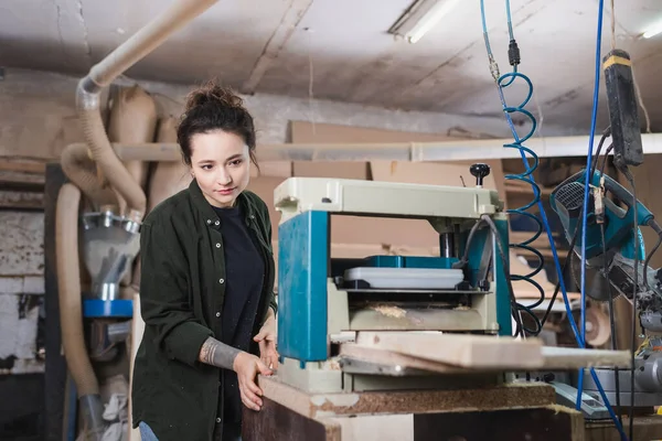 Brünette Holzarbeiterin steht neben Dickenhobelmaschine in Werkstatt — Stockfoto