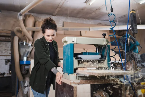 Young furniture designer looking at bench thicknesser and plank in workshop — Stock Photo