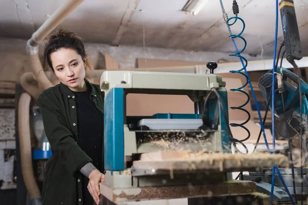 Brunette charpentier regardant la sciure de bois dans raboteuse épaisseur — Photo de stock