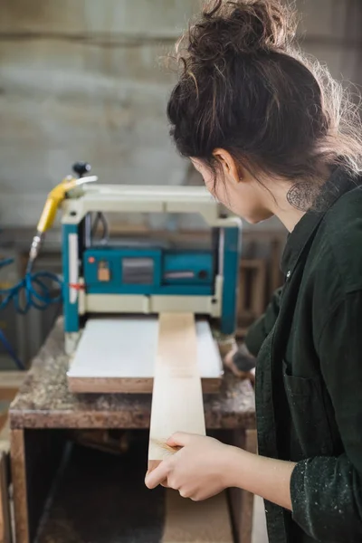 Tattooed carpenter holding blurred plank near bench thicknesser on background — Stock Photo