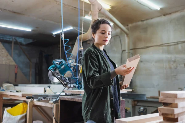 Jeune menuisier tenant une planche en bois dans un atelier — Photo de stock