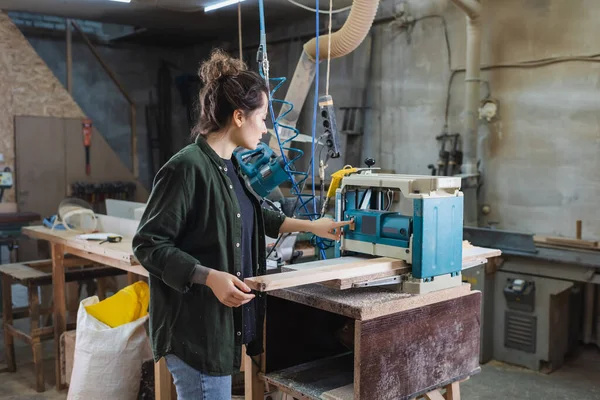 Side view of brunette carpenter turning on thickness planer in workshop — Stock Photo