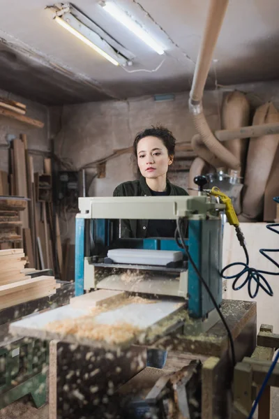 Carpenter standing near thickness planer and blurred sawdust in workshop — Stock Photo