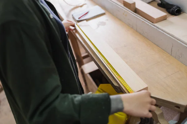 Обрезанный вид плотника, держащего рулетку возле деревянной доски в мастерской — стоковое фото