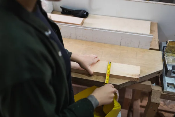 Cropped view of furniture designer measuring wooden plank in workshop — Stock Photo