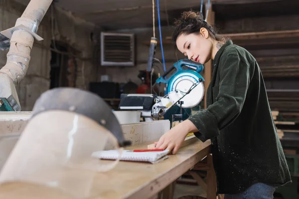 Carpenter measuring wooden plank near blurred safety visor in workshop — Stock Photo