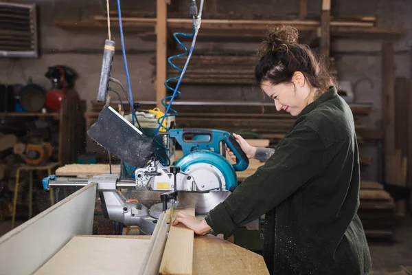 Seitenansicht des lächelnden Tischlers mit der Gehrungssäge in der Werkstatt — Stockfoto