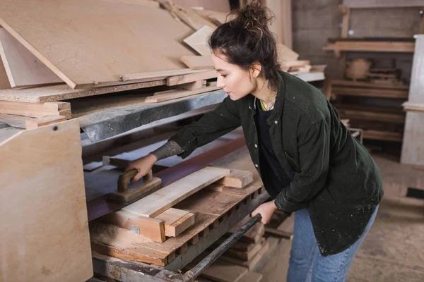 Side view of tattooed carpenter polishing wooden plank in workshop — Stock Photo