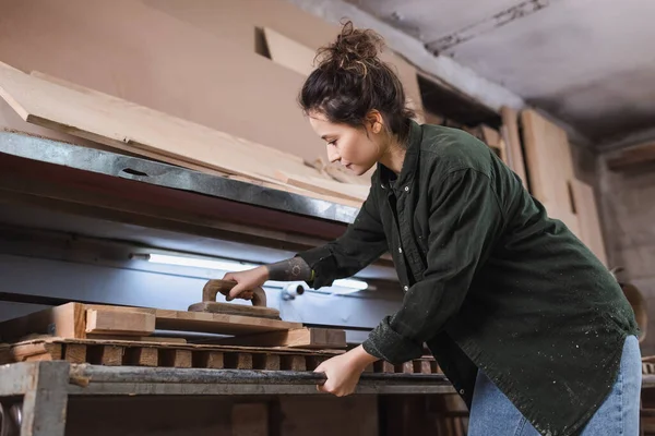 Side view of brunette carpenter polishing wooden planks in workshop — Stock Photo