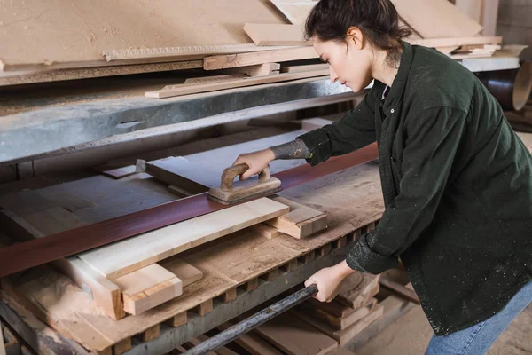 Side view of tattooed carpenter in sawdust polishing plank in workshop — Stock Photo