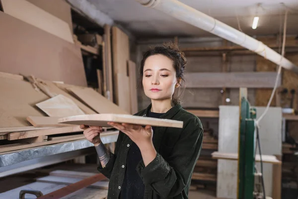 Junger Tischler hält verschwommenes Holzbrett in Werkstatt — Stockfoto