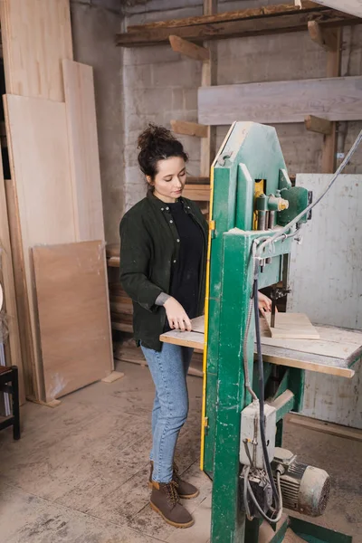 Carpentiere che tiene la tavola di legno mentre lavora alla sega a nastro in officina — Foto stock