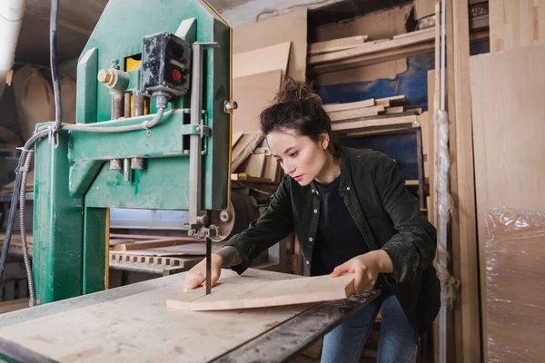 Carpenter holding wooden planks near band saw in workshop — Stock Photo