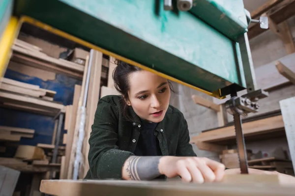 Young tattooed carpenter working in band saw in workshop — Stock Photo