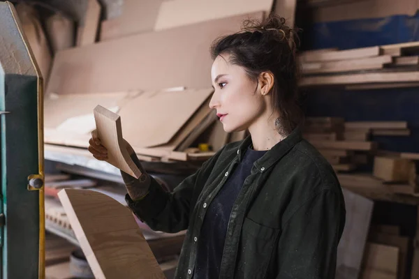 Vue latérale du charpentier tatoué tenant une planche en bois dans l'atelier — Photo de stock
