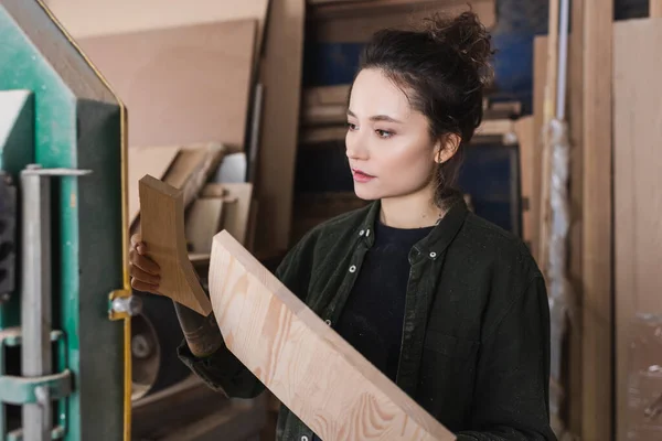 Junge Möbeldesignerin im Hemd hält Holzplanken in Werkstatt — Stockfoto