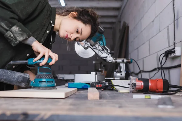 Carpenter using sander on wooden plank in workshop — Stock Photo