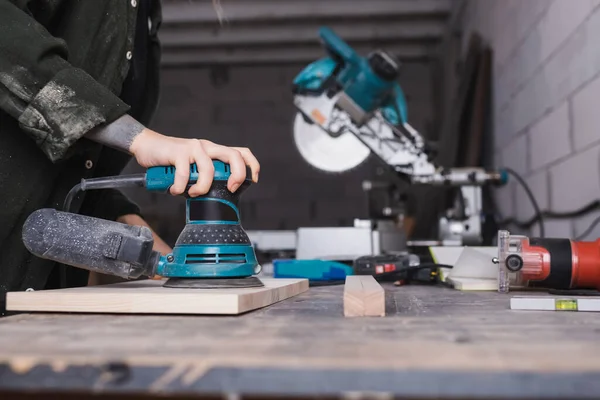 Cropped view of furniture designer using sander on wooden board in workshop — Stock Photo