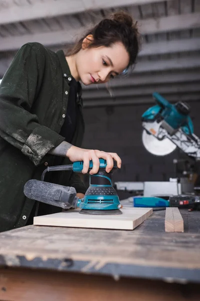 Blurred carpenter using sander while polishing plank in workshop — Stock Photo