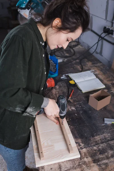 Vista lateral de tablones de madera de perforación de carpintero en taller - foto de stock