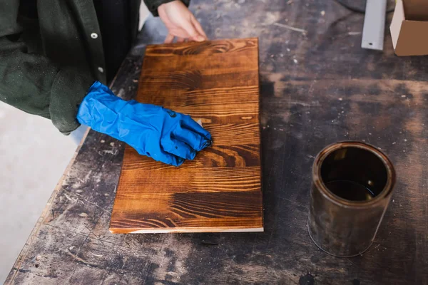 Top view of woodworker applying wood stain on board near jar in workshop — Stock Photo