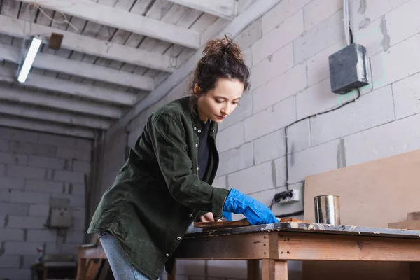 Carpenter in shirt and rubber glove applying wood stain on plank in workshop — Stock Photo