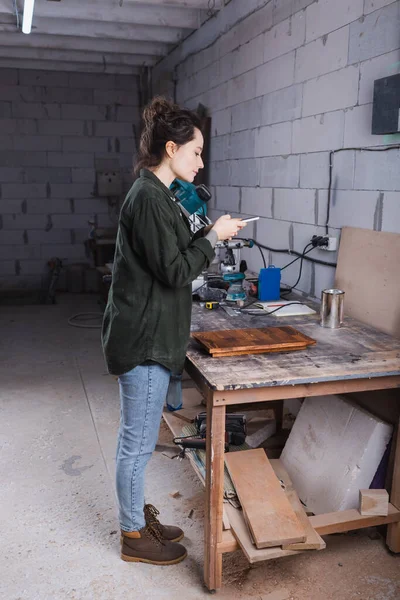 Вид сбоку дизайнера мебели, делающего фото на мобильный телефон возле доски в мастерской — стоковое фото