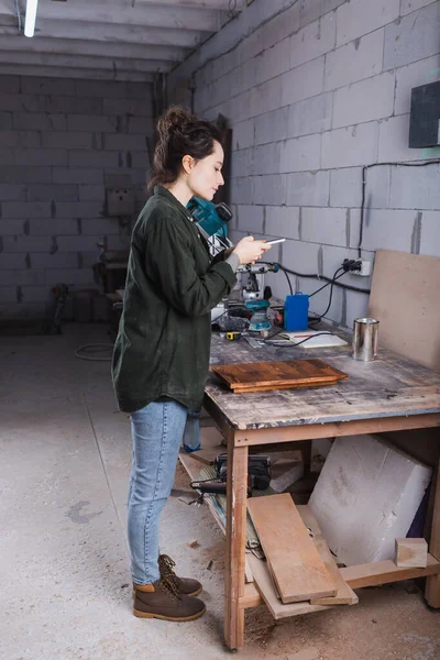 Vue latérale du designer de meubles prenant des photos sur téléphone portable près de la planche dans l'atelier — Photo de stock