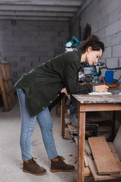 Vue latérale du designer de meubles écrivant sur ordinateur portable dans l'atelier — Photo de stock