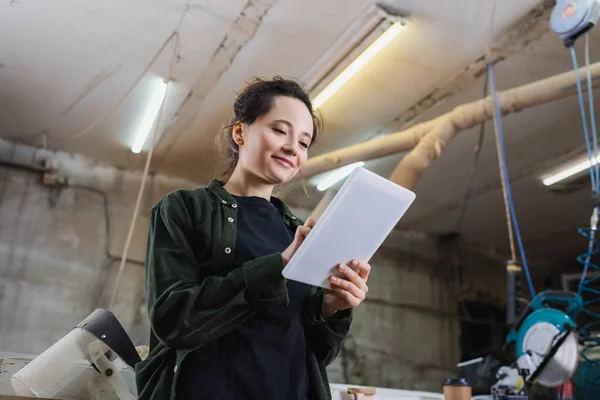 Vue à faible angle du jeune menuisier à l'aide d'une tablette numérique près d'une visière de sécurité en atelier — Photo de stock