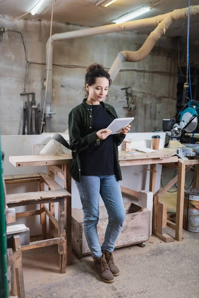 Carpenter holding digital tablet near visor and coffee to go in workshop — Stock Photo