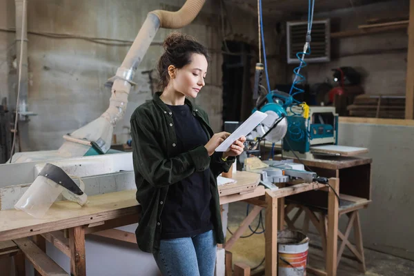 Brunette carpenter using digital tablet near protective visor and equipment in workshop — Stock Photo