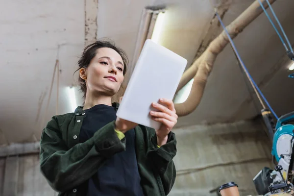 Low angle view of brunette carpenter using digital tablet in workshop — Stock Photo