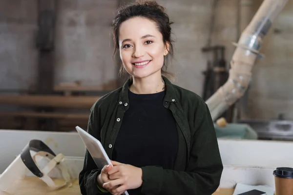 Cheerful carpenter holding digital tablet in workshop — Stock Photo
