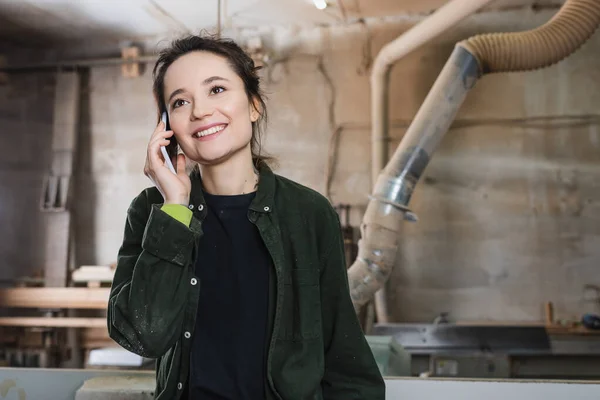 Happy woodworker talking on mobile phone in workshop — Stock Photo