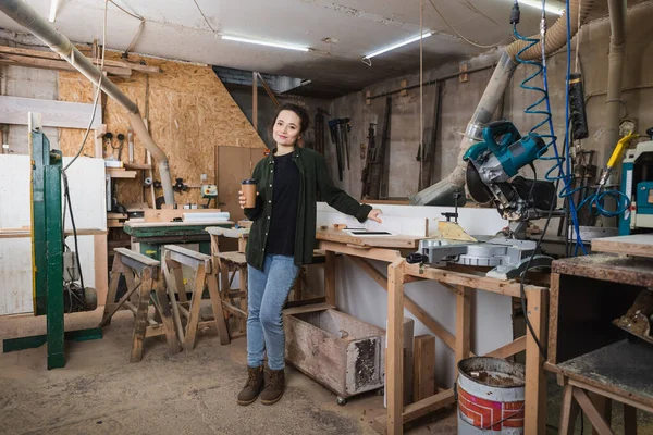 Tischler hält Pappbecher in der Nähe von Geräten und Geräten in Werkstatt — Stockfoto