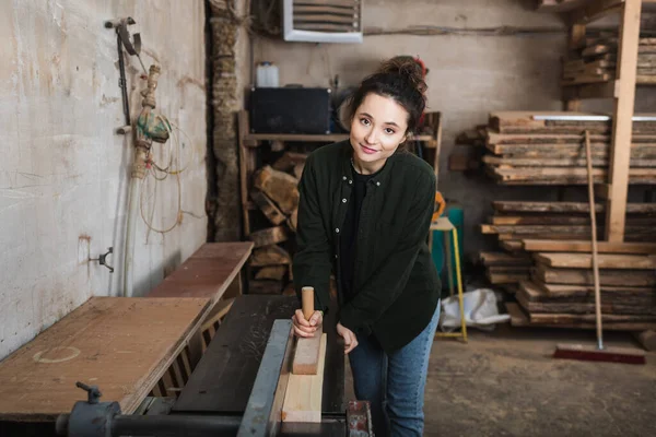 Charpentier souriant regardant la caméra tout en travaillant sur la machine à menuisier — Photo de stock