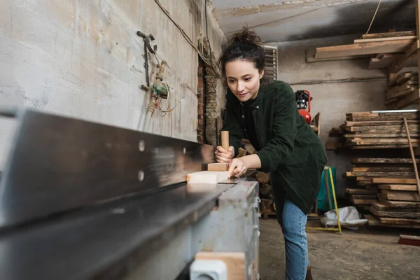 Brünette Möbeldesignerin arbeitet in verschwommener Werkstatt an Tischler-Maschine — Stockfoto