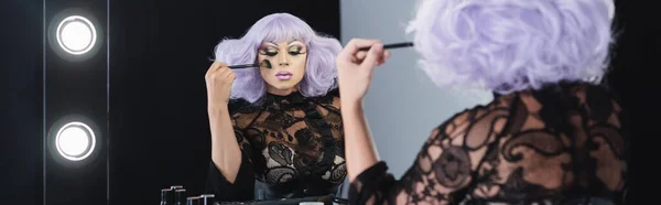 Eccentric man in purple wig applying face powder near mirror, banner — Stock Photo