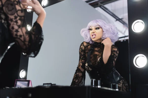 Low angle view of drag queen in purple wig grimacing while looking in mirror — Stock Photo