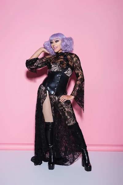 Lächelnde Drag Queen im Glamour-Kleid, das die Haare fixiert, während sie auf rosa wegschaut — Stockfoto