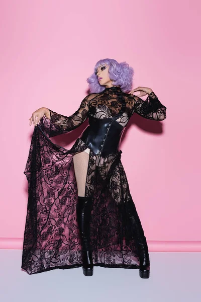 Vue pleine longueur de drag queen tenant robe en dentelle noire tout en regardant loin sur rose — Photo de stock