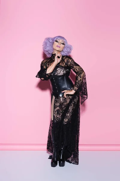 Piena lunghezza vista di drag queen toccando mento mentre posa con mano sul fianco su rosa — Foto stock