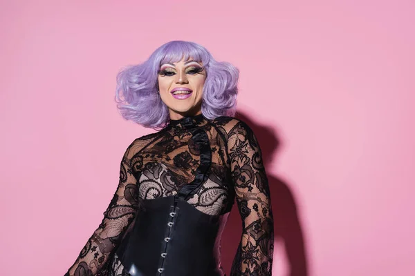 Eccentric man in purple wig and black lace clothing smiling at camera on pink — Stock Photo