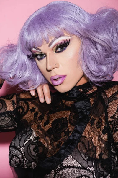 Man in purple wig and black lace clothes looking at camera on pink — Stock Photo