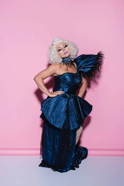 Excéntrica drag queen con maquillaje brillante posando con la mano en la cadera en rosa - foto de stock