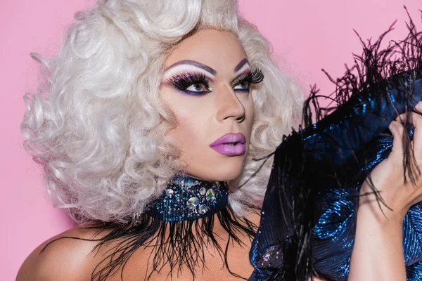 Excéntrica drag queen con maquillaje brillante mirando hacia otro lado aislado en rosa - foto de stock