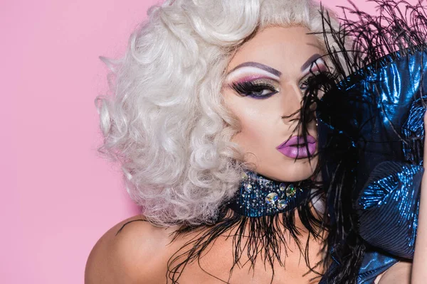 Extravagant drag queen looking at camera near feather boa isolated on pink — Stock Photo