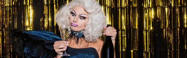 Drag queen with bottle and glass of champagne pouting lips on shiny background, banner — Stock Photo